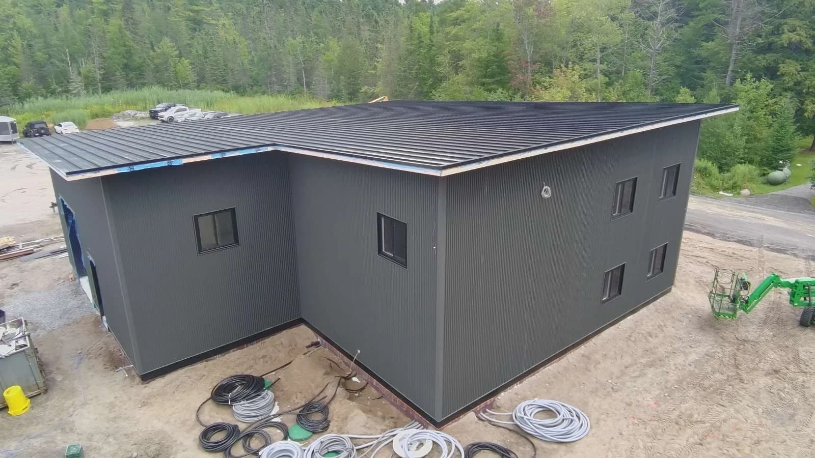 Rear aerial view of a building with dark metal siding and a low-slope metal roof