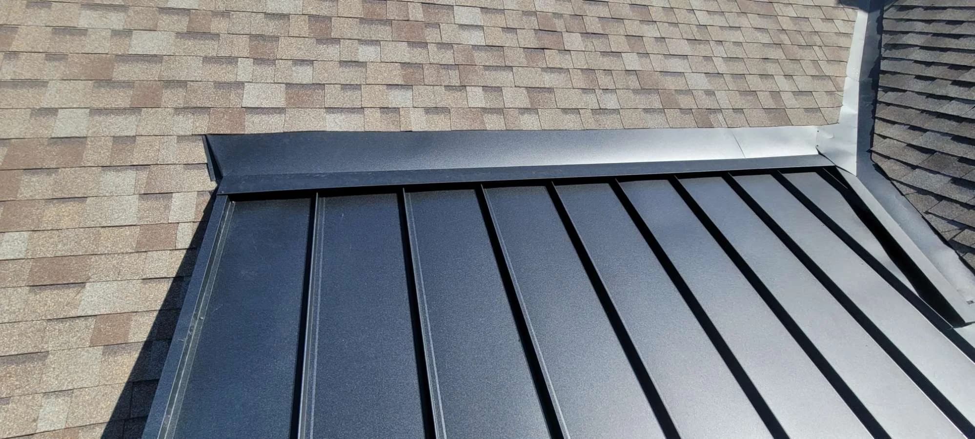 Dark standing seam roof meeting a shingled roof at a wall