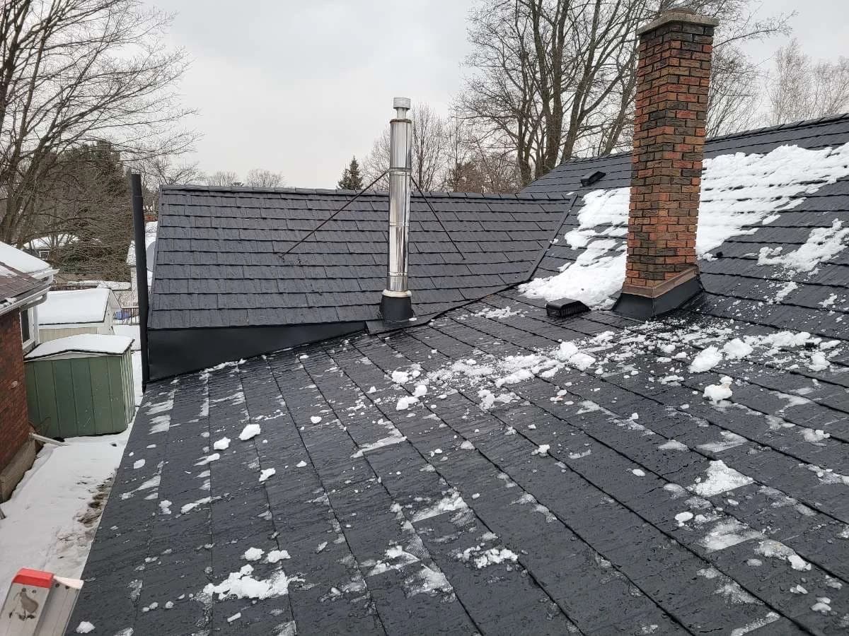 Metal shingle roof meeting a brick chimney in winter